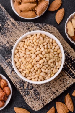 Koyu beton arka planda bir kasede soyulmuş çam fıstığı. Protein kaynağı olarak fındık.