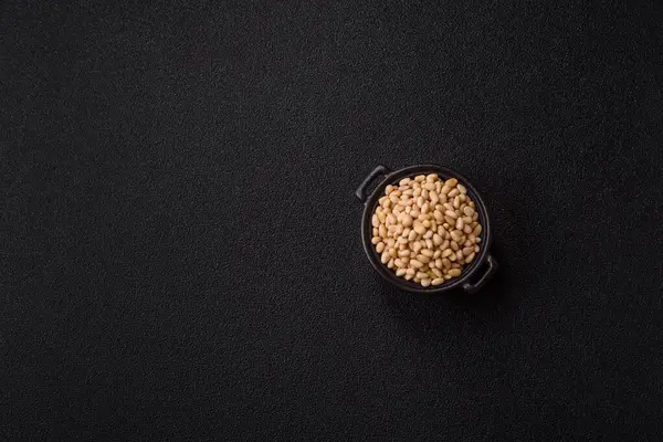 Koyu beton arka planda bir kasede soyulmuş çam fıstığı. Protein kaynağı olarak fındık.