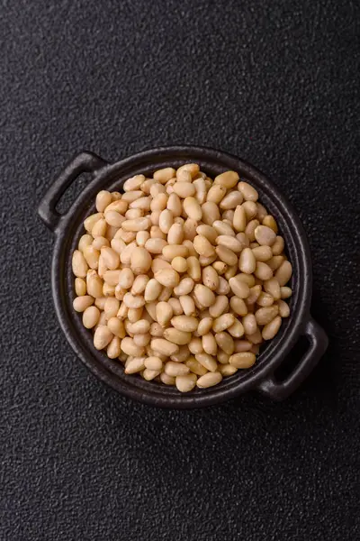 Koyu beton arka planda bir kasede soyulmuş çam fıstığı. Protein kaynağı olarak fındık.