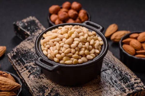 Koyu beton arka planda bir kasede soyulmuş çam fıstığı. Protein kaynağı olarak fındık.