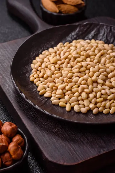 Koyu beton arka planda bir kasede soyulmuş çam fıstığı. Protein kaynağı olarak fındık.