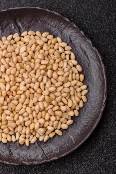 Koyu beton arka planda bir kasede soyulmuş çam fıstığı. Protein kaynağı olarak fındık.