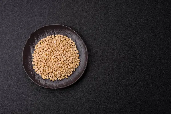 Koyu beton arka planda bir kasede soyulmuş çam fıstığı. Protein kaynağı olarak fındık.