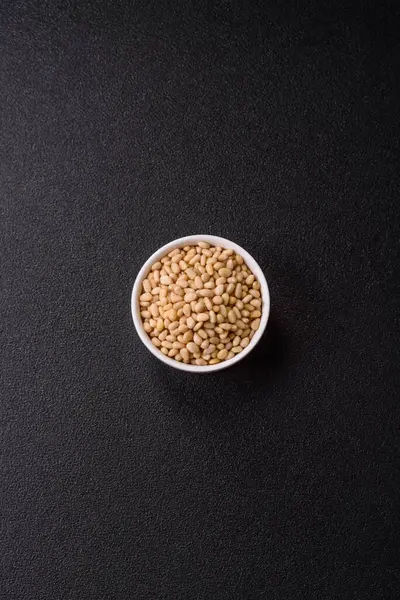 Koyu beton arka planda bir kasede soyulmuş çam fıstığı. Protein kaynağı olarak fındık.