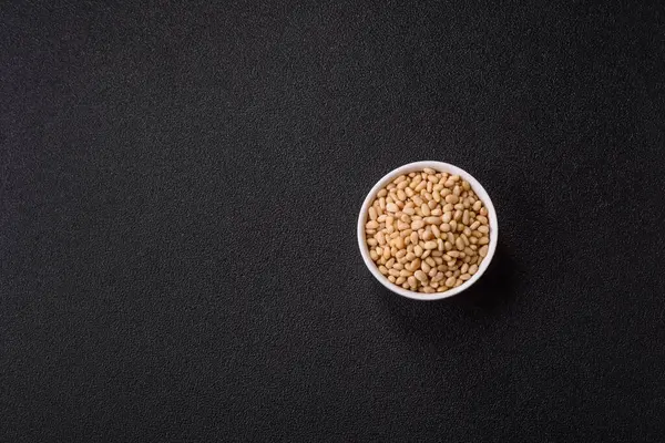 Koyu beton arka planda bir kasede soyulmuş çam fıstığı. Protein kaynağı olarak fındık.