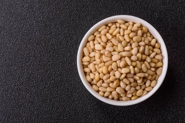 Koyu beton arka planda bir kasede soyulmuş çam fıstığı. Protein kaynağı olarak fındık.