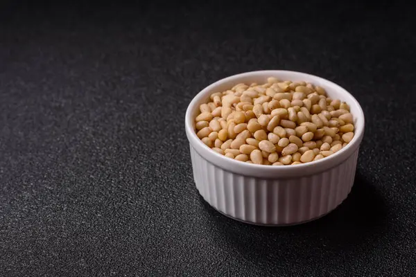 Koyu beton arka planda bir kasede soyulmuş çam fıstığı. Protein kaynağı olarak fındık.