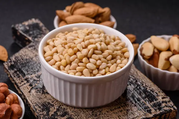 Koyu beton arka planda bir kasede soyulmuş çam fıstığı. Protein kaynağı olarak fındık.