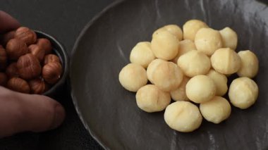 Koyu beton arka planda seramik kasede soyulmuş macadamia cevizi. Besin kaynağı olarak fındık