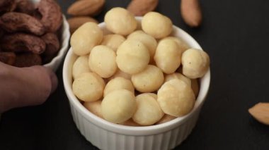 Koyu beton arka planda seramik kasede soyulmuş macadamia cevizi. Besin kaynağı olarak fındık
