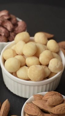 Koyu beton arka planda seramik kasede soyulmuş macadamia cevizi. Besin kaynağı olarak fındık