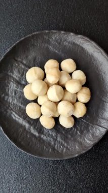 Koyu beton arka planda seramik kasede soyulmuş macadamia cevizi. Besin kaynağı olarak fındık