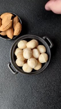 Koyu beton arka planda seramik kasede soyulmuş macadamia cevizi. Besin kaynağı olarak fındık