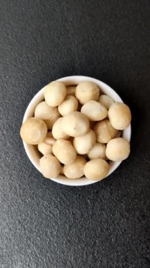 Koyu beton arka planda seramik kasede soyulmuş macadamia cevizi. Besin kaynağı olarak fındık