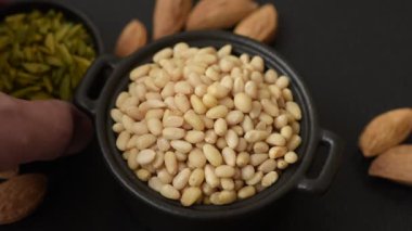 Koyu beton arka planda bir kasede soyulmuş çam fıstığı. Protein kaynağı olarak fındık.