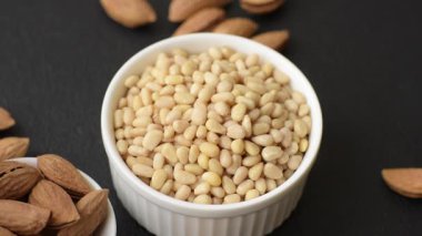 Koyu beton arka planda bir kasede soyulmuş çam fıstığı. Protein kaynağı olarak fındık.