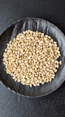 Koyu beton arka planda bir kasede soyulmuş çam fıstığı. Protein kaynağı olarak fındık.