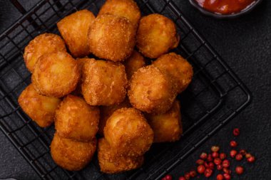 Peynir ya da patates kroketleri, tuzlu ekmekle kızartılmış toplar, koyu beton arka planda baharatlar.