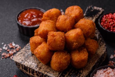 Peynir ya da patates kroketleri, tuzlu ekmekle kızartılmış toplar, koyu beton arka planda baharatlar.