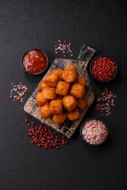 Peynir ya da patates kroketleri, tuzlu ekmekle kızartılmış toplar, koyu beton arka planda baharatlar.