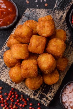 Peynir ya da patates kroketleri, tuzlu ekmekle kızartılmış toplar, koyu beton arka planda baharatlar.