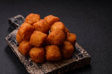 Peynir ya da patates kroketleri, tuzlu ekmekle kızartılmış toplar, koyu beton arka planda baharatlar.