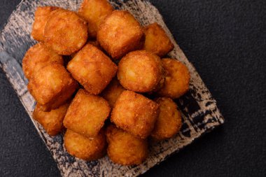 Peynir ya da patates kroketleri, tuzlu ekmekle kızartılmış toplar, koyu beton arka planda baharatlar.