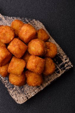 Peynir ya da patates kroketleri, tuzlu ekmekle kızartılmış toplar, koyu beton arka planda baharatlar.