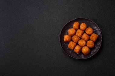 Peynir ya da patates kroketleri, tuzlu ekmekle kızartılmış toplar, koyu beton arka planda baharatlar.