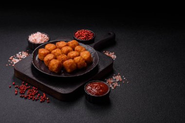 Peynir ya da patates kroketleri, tuzlu ekmekle kızartılmış toplar, koyu beton arka planda baharatlar.