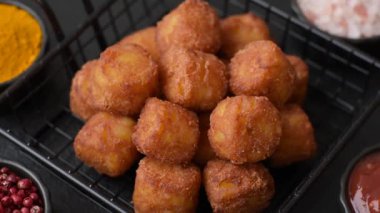 Peynir ya da patates kroketleri, tuzlu ekmekle kızartılmış toplar, koyu beton arka planda baharatlar.