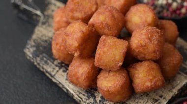 Peynir ya da patates kroketleri, tuzlu ekmekle kızartılmış toplar, koyu beton arka planda baharatlar.