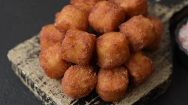 Peynir ya da patates kroketleri, tuzlu ekmekle kızartılmış toplar, koyu beton arka planda baharatlar.