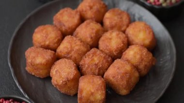Peynir ya da patates kroketleri, tuzlu ekmekle kızartılmış toplar, koyu beton arka planda baharatlar.