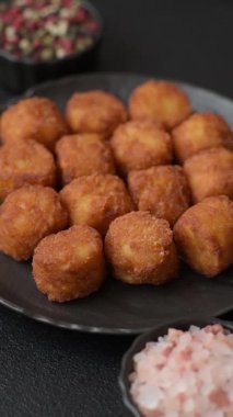 Peynir ya da patates kroketleri, tuzlu ekmekle kızartılmış toplar, koyu beton arka planda baharatlar.