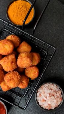 Peynir ya da patates kroketleri, tuzlu ekmekle kızartılmış toplar, koyu beton arka planda baharatlar.