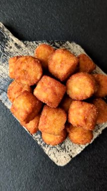 Peynir ya da patates kroketleri, tuzlu ekmekle kızartılmış toplar, koyu beton arka planda baharatlar.