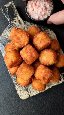 Peynir ya da patates kroketleri, tuzlu ekmekle kızartılmış toplar, koyu beton arka planda baharatlar.