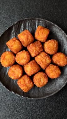 Peynir ya da patates kroketleri, tuzlu ekmekle kızartılmış toplar, koyu beton arka planda baharatlar.