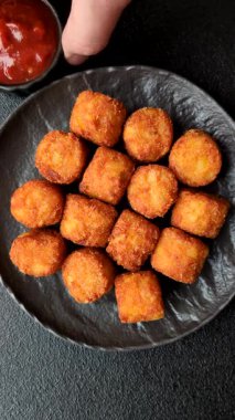 Peynir ya da patates kroketleri, tuzlu ekmekle kızartılmış toplar, koyu beton arka planda baharatlar.