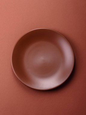 Tek renkli kahverengi arka planda boş seramik plaka. Yemek masasında çatal bıçak takımı olan boş bir tabak.