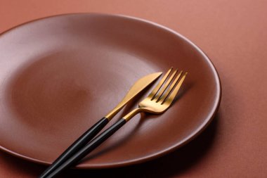 Tek renkli kahverengi arka planda boş seramik plaka. Yemek masasında çatal bıçak takımı olan boş bir tabak.