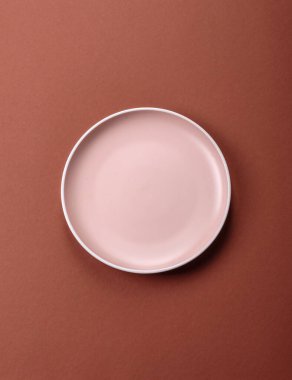 Tek renkli kahverengi arka planda boş seramik plaka. Yemek masasında çatal bıçak takımı olan boş bir tabak.