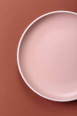Tek renkli kahverengi arka planda boş seramik plaka. Yemek masasında çatal bıçak takımı olan boş bir tabak.