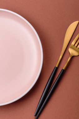 Tek renkli kahverengi arka planda boş seramik plaka. Yemek masasında çatal bıçak takımı olan boş bir tabak.