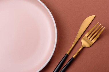 Tek renkli kahverengi arka planda boş seramik plaka. Yemek masasında çatal bıçak takımı olan boş bir tabak.