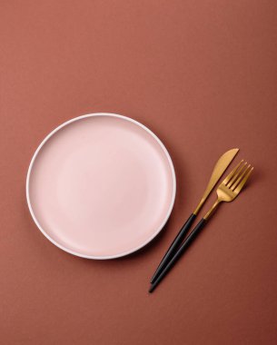 Tek renkli kahverengi arka planda boş seramik plaka. Yemek masasında çatal bıçak takımı olan boş bir tabak.