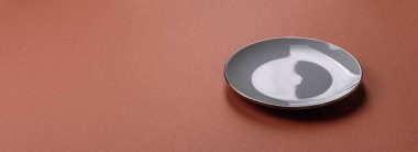 Tek renkli kahverengi arka planda boş seramik plaka. Yemek masasında çatal bıçak takımı olan boş bir tabak.