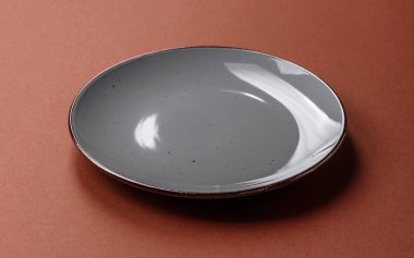 Tek renkli kahverengi arka planda boş seramik plaka. Yemek masasında çatal bıçak takımı olan boş bir tabak.