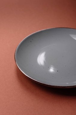 Tek renkli kahverengi arka planda boş seramik plaka. Yemek masasında çatal bıçak takımı olan boş bir tabak.